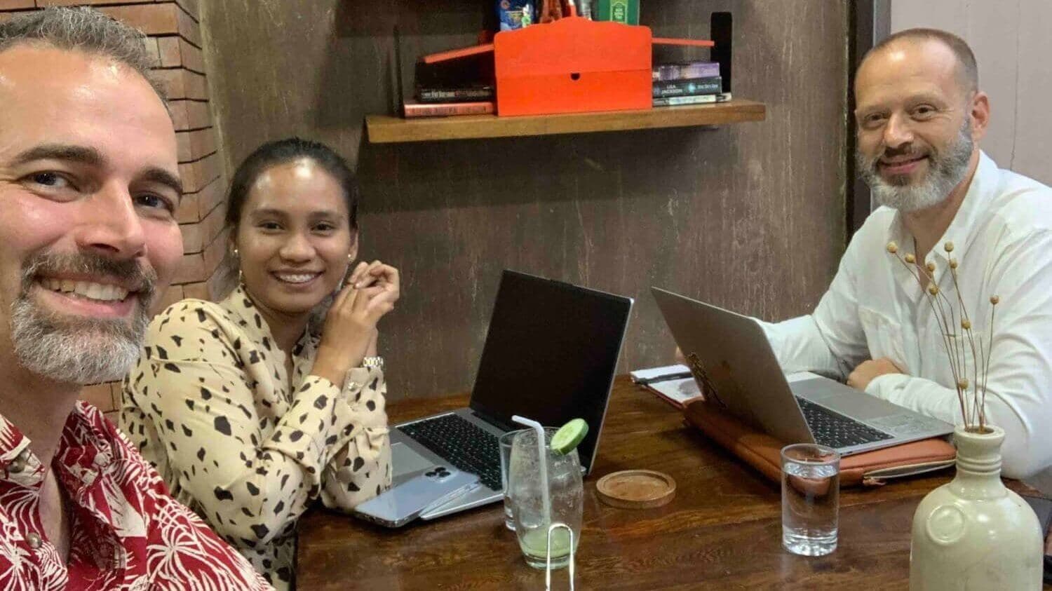 Isaac, Daisy and Jason smiling at a café table with their laptops open